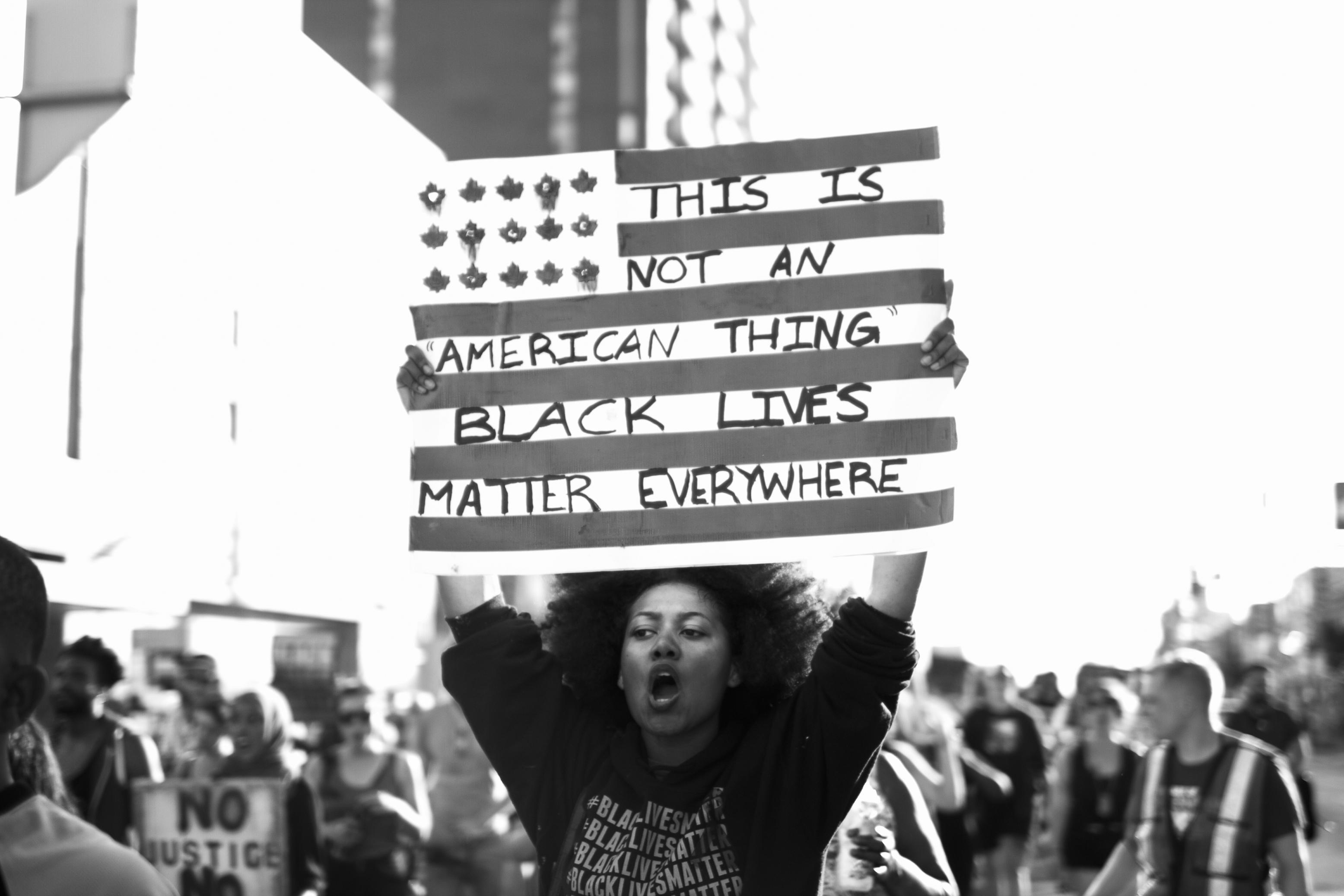 Jalani Morgan: Untitled, Toronto (2015). Anti-Blackness is global, as is our resistance. A marcher at a 2015 protest raises a sign to reinforce that state violence and oppression isn’t exclusive to America.